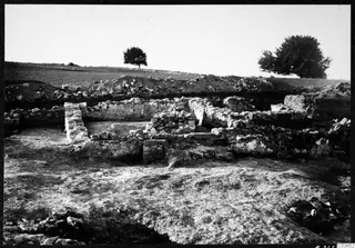 Excavated stone walls of the Cholades temples A-B at Soli, with rubble heaps and trees on the skyline
