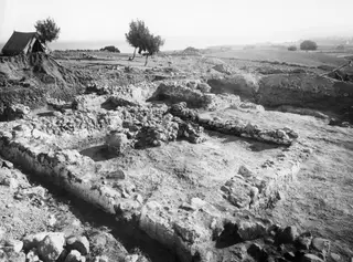 Excavated stone walls of Room V at Soli, seen from the west, with a tent and trees behind.