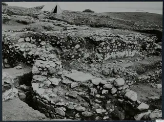 Excavated stone walls at Soli, Cholades, with a white tent on the hill and the sea beyond