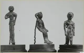 Three small bronze figurines on wooden bases: two standing figures and one seated figure leaning to the side