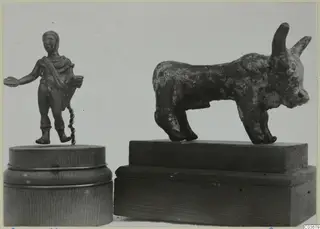 Two small bronze figures on wooden bases: a standing human figure holding a dish, and a horned bronze bull.