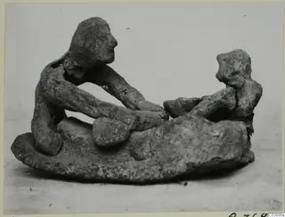 Terracotta figurine group of two figures on a rounded base, one seated and reaching toward the other