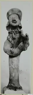 Terracotta figurine of a standing figure with bent arms and a wide cap-like headdress, set on a plinth