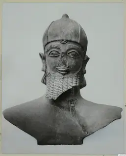 Terracotta bust of a bearded figure in a rounded cap with a small knob on top, shown against a plain background.
