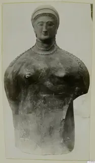 Bust of a woman with a cap-like headdress and beaded necklace, seen frontally against a pale background, from Vouni