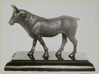 Bronze statuette of a standing bull facing left, mounted on a dark wooden base.
