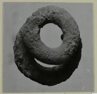 Silver object from Vouni: a ring-shaped find with a large central hole and a rough, dark, corroded surface.
