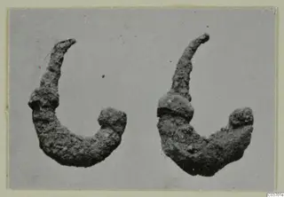 Two corroded, curved metal objects with knobbed ends, photographed side by side on a grey background