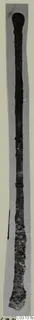 Long slender bronze implement with a rounded head, photographed upright against grey, from Vouni.