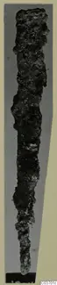 Corroded iron tool from Vouni, long and narrow, tapering toward a blunt end at the bottom.