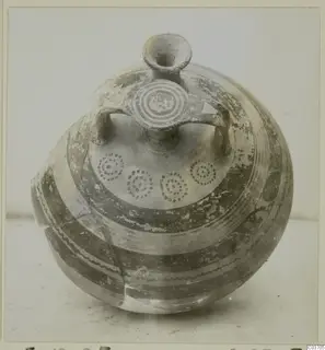 Round-bodied pottery vessel with a tall neck, two handles and painted bands and concentric circle motifs, photographed on a plain surface.