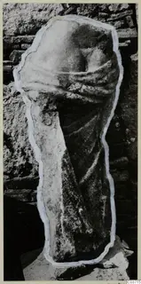 Back view of a draped marble statue fragment from Galini, standing against a stone wall