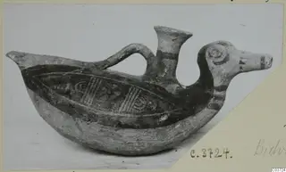 Painted pottery bird-shaped vessel with a flared spout, a loop handle and dark painted bands on a pale body.