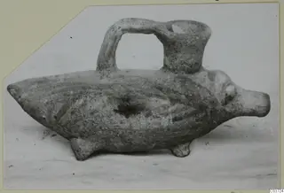 Pottery vessel shaped like a stocky animal, with a loop handle rising from its back to a cup-shaped opening, photographed on a card mount