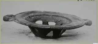 Shallow pottery bowl with two projecting lug handles, standing on a perforated openwork base, seen from the side