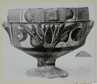 Footed pottery vessel with two side lugs and black painted bands, spirals and leaf-like motifs on a pale ground