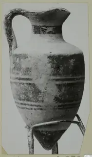 Jug with a single strap handle and dark painted horizontal bands, shown on a thin wire stand.