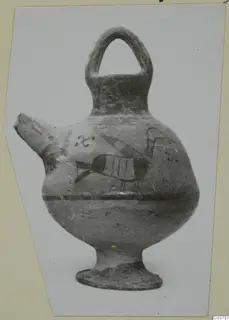 Painted pottery vessel with a strap handle and a broken spout, with a bird-like motif on the body, photographed on a card mount