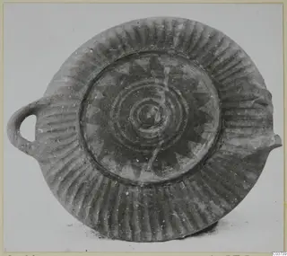 Shallow pottery dish with a loop handle, radial fluting on the rim and a painted star and concentric circles in the centre