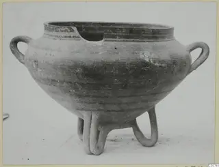 Round pottery vessel with two loop handles and three tubular feet, rim broken at the front