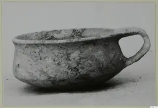 Plain white wheel-made bowl with a single loop handle, seen from the side.