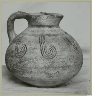 Round-bellied jug with a loop handle and dark spiral motifs painted on its body.