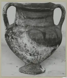 Two-handled pottery vessel with black slip and a pedestal foot, photographed from the front