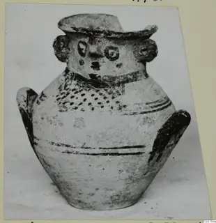 Pottery jug with a modelled face on the neck and painted dark bands, shown on a card mount