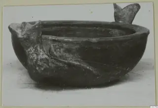 Grey polished ware bowl with two projecting lugs, photographed on a pale surface