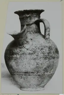 Pottery jug with a pinched spout, strap handle and horizontal bands, photographed on a card mount