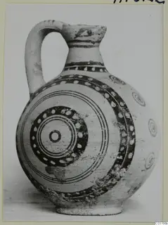 Painted pottery jug with a strap handle and concentric circle decoration, shown on a card mount