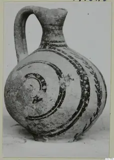 Painted pottery jug with a strap handle, dark bands and spirals with white dots on a pale body