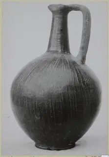 Black-burnished jug with a tall neck, single strap handle and stroke-polished surface, photographed against a plain background.