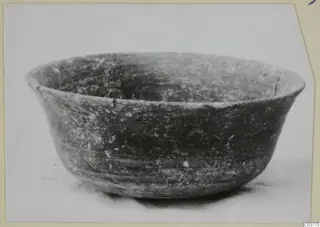 Dark bowl with a flared rim, photographed from the side on a pale surface