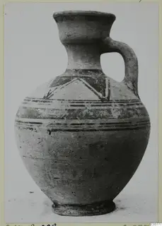 Painted jug with a high collar neck, one loop handle and bands of dark paint with a zigzag motif on the shoulder.