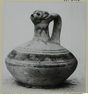 Pottery jug with a rounded body, strap handle and dark painted bands, shown on a plain background