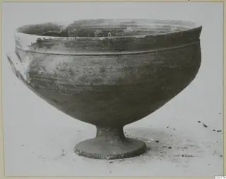 Footed bowl with two small side handles, photographed in profile on a pale surface.