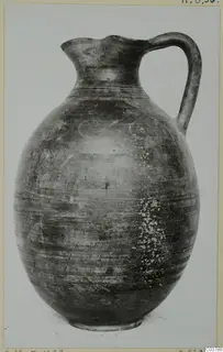 Tall jug with a wide globular body, a trefoil-style mouth and a strap handle, photographed against a plain background