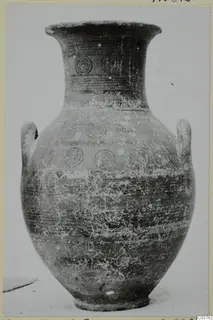 Pottery vessel with two handles and concentric circle motifs, photographed upright on a pale surface, Black-on-Red I-III.