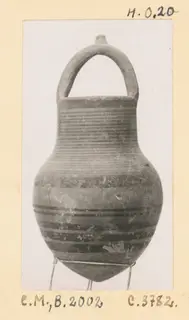 Black-on-Red pottery jug with a loop handle, ribbed neck and dark painted bands, photographed on a wire stand