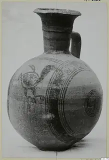 Bichrome IV jug with a globular body, tall flaring neck and loop handle, painted with concentric circles and a bird-like motif.