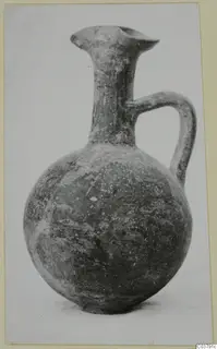 Round-bodied jug with a tall narrow neck, flared lip and strap handle, photographed against a pale background