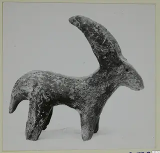 Small figurine of a horned animal standing on four legs, with a long curved horn and a mottled dark surface.