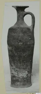 Pottery amphora with a single handle, a flared rim and a tall body, shown against a pale background
