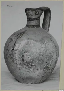 Round-bodied jug with a single loop handle and dark painted bands on the neck, shown on a plain surface.