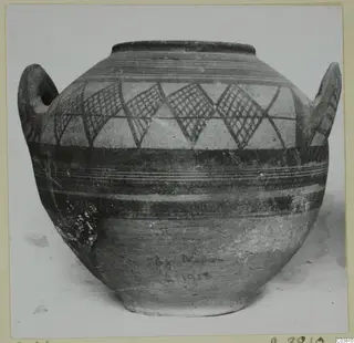 Painted two-handled jug with lattice-filled triangles and horizontal bands, photographed against a pale background