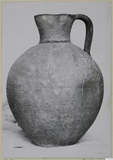 Round-bodied jug with a tall flared neck and a single strap handle, photographed against a plain background.