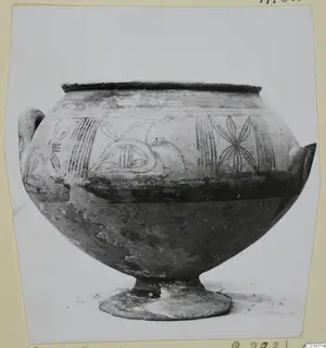 Painted pottery vessel with a wide body, two small handles and a short footed base, shown in a photograph mounted on a card.