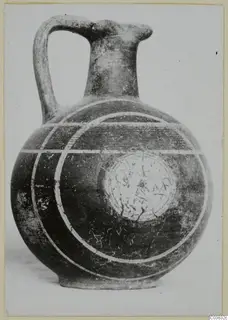 Jug with a strap handle and a globular body, its dark surface marked with pale painted bands and concentric arcs