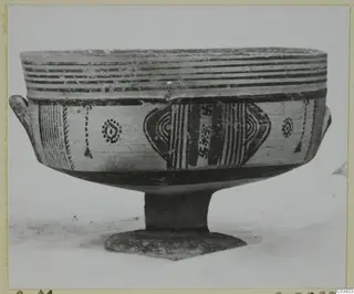 Painted pottery stemmed bowl with two small handles, black bands and motifs on a cream surface